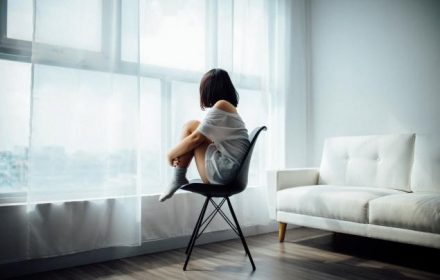 girl sitting on chair looking out window, coping with loneliness