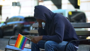 coming out - worried man sitting on bench holding rainbow flag