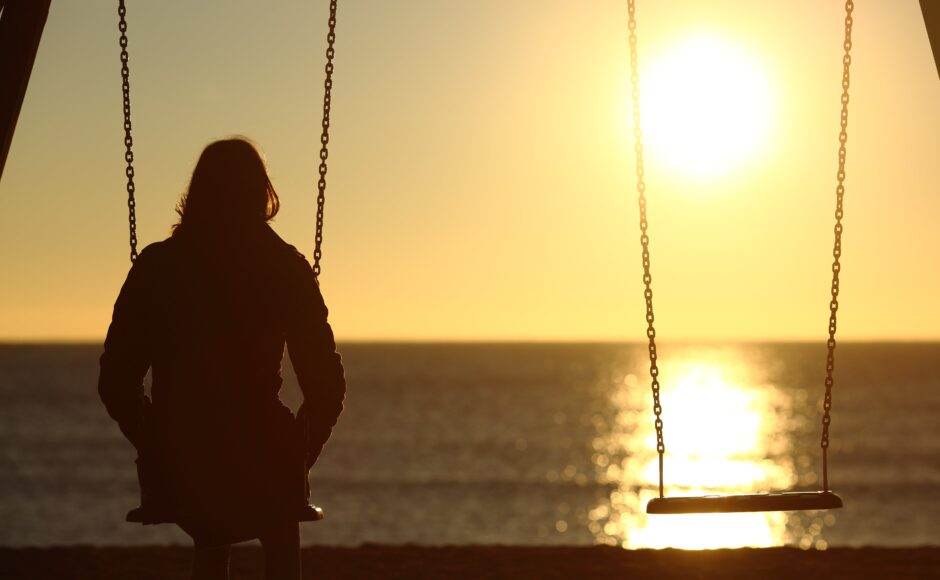 Loneliness and mental health. Woman sitting on swing at sunset with empty swing next to her.